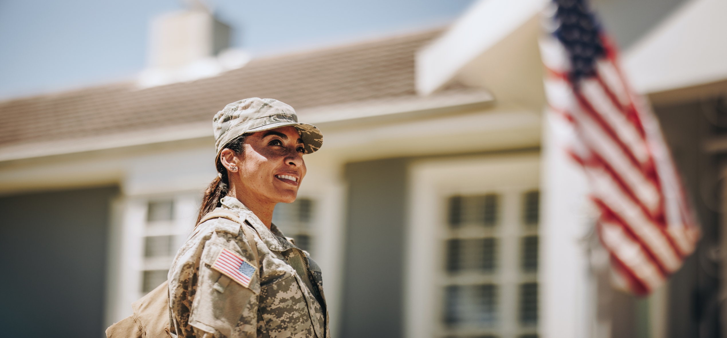 Servicewoman standing in front of her home with American flag in the background